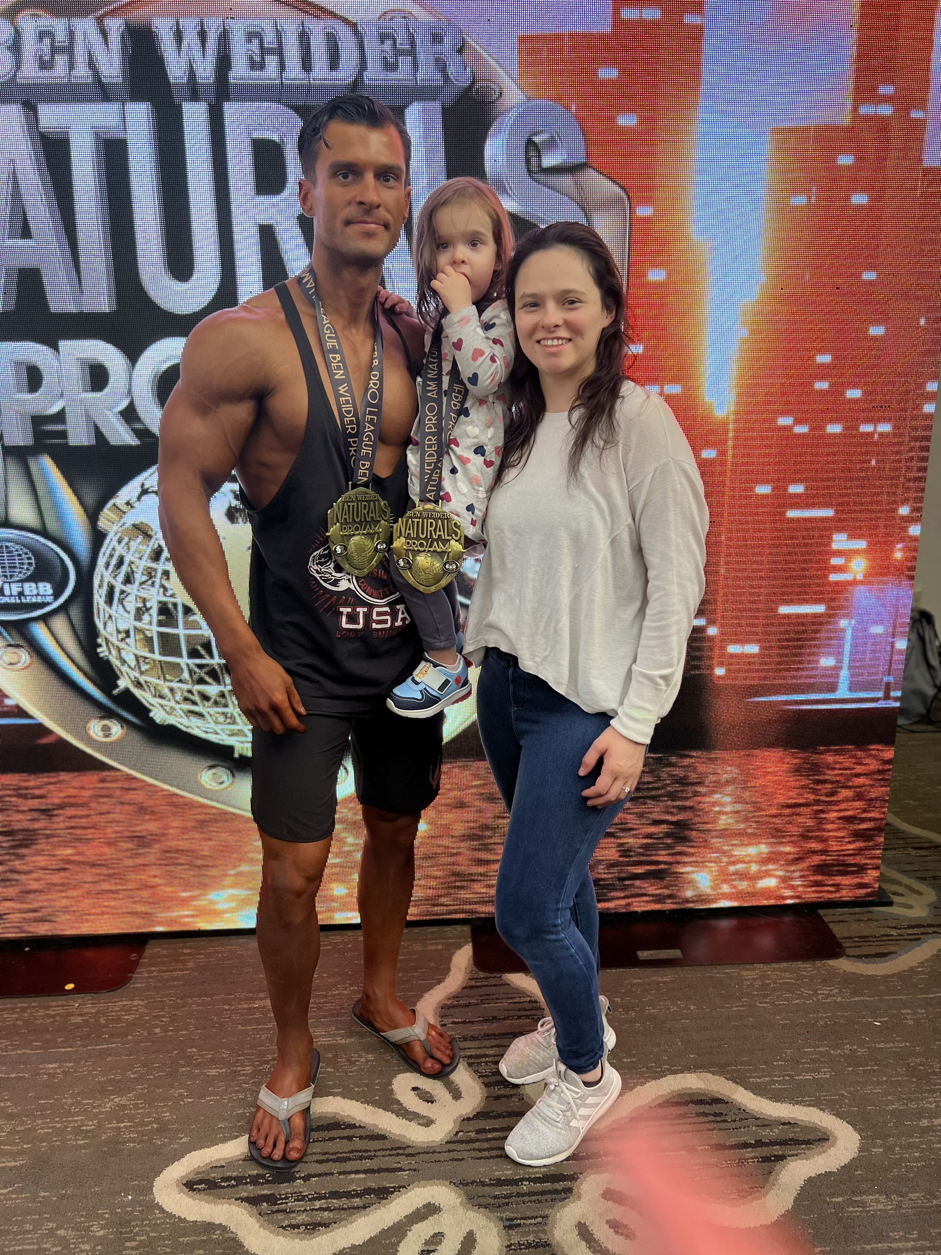 Peyton Jones with his wife and daughter, holding his two men's physique championship medals